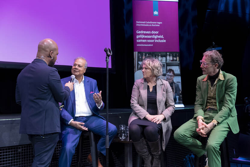 Van links naar rechts staan Winston Brandon (met zijn rug naar de camera), Rabin Baldewsingh, wethouder Schuttenbeld van Zwolle en Sjaak van der Linde op een podium. Winston interviewt Rabin.